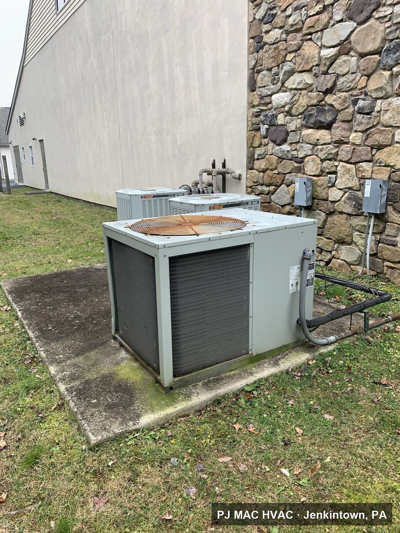 Ground-mounted commercial HVAC units serviced by PJ MAC HVAC beside a stone building in the Philadelphia area.