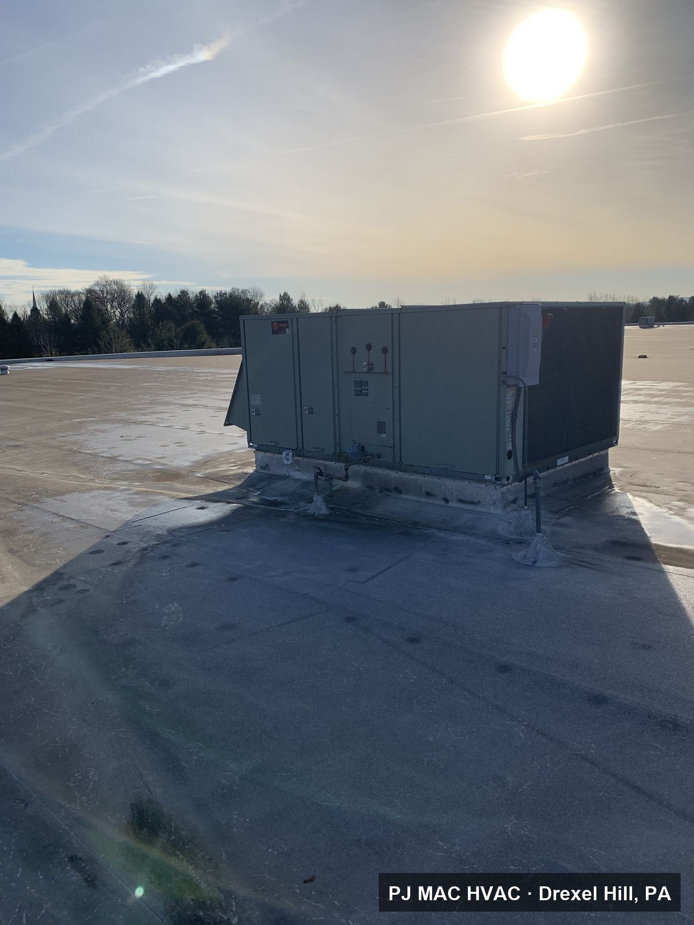 A Trane commercial rooftop unit serviced by PJ MAC HVAC on a large flat roof in winter.